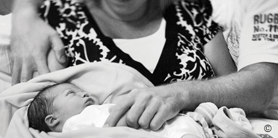 Baby ligt op schoot moeder met troostende hand van vader.